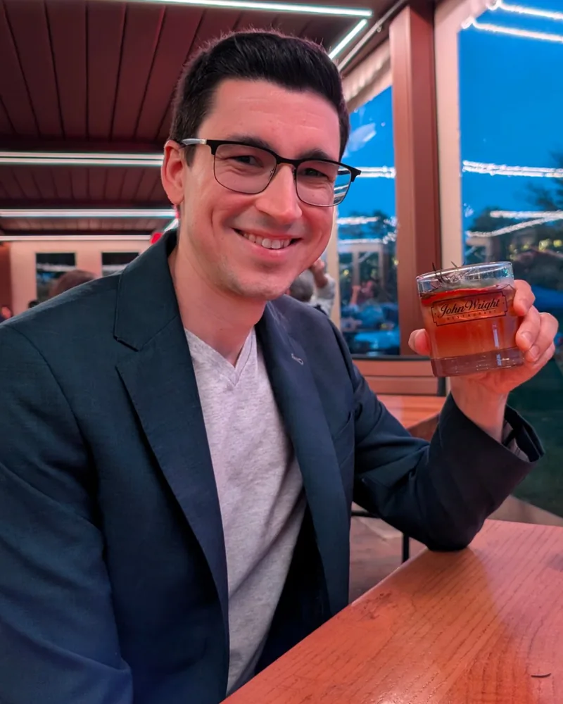 Greg Lauver smiling, holding a drink at an evening patio table